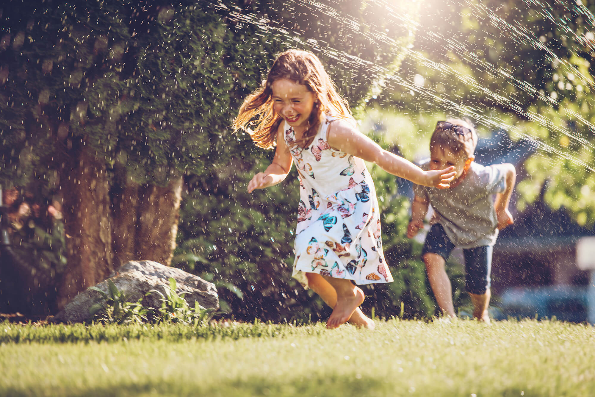 a young boy and girl running through a sprinkler on a lawn