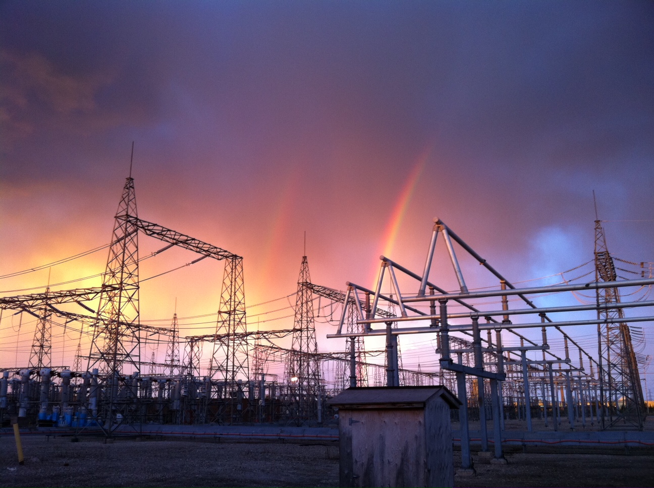 Photo of a Hydro One transmission station during a rain storm with a double rainbow behind it