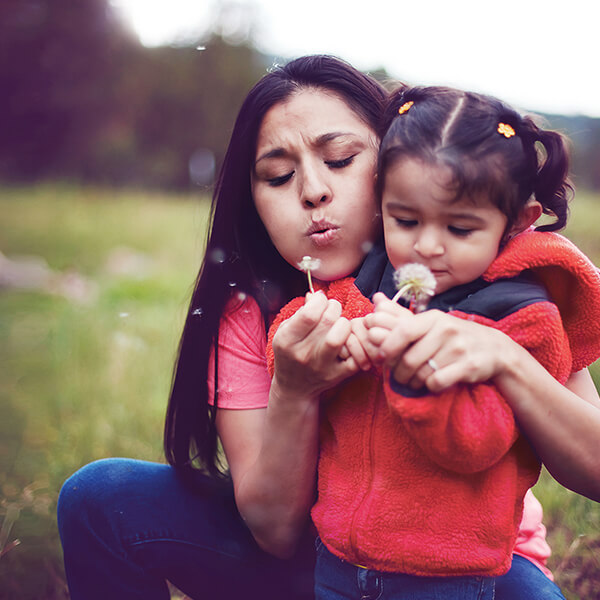 Photo of a woman and her daughter blowing dandelion petals