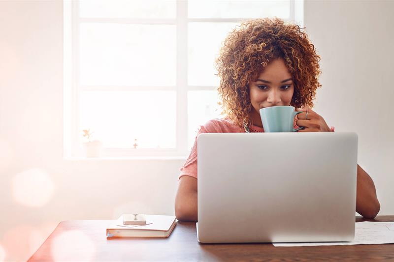 photo of a woman drinking coffee while using a laptop