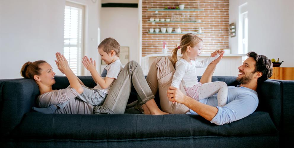 photo of a mother and father playing with their son and daughter on the couch