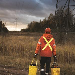image of a Hydro One forestry management worker carrying equipment down a transmission right-of-way