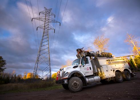 photo of a Hydro One bucket truck with a transmission tower in the background