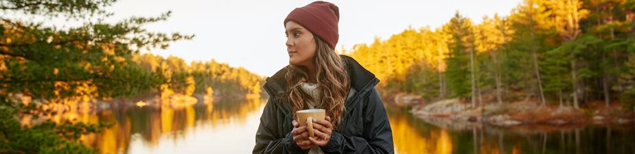 Image of a woman holding a mug, standing by a lake