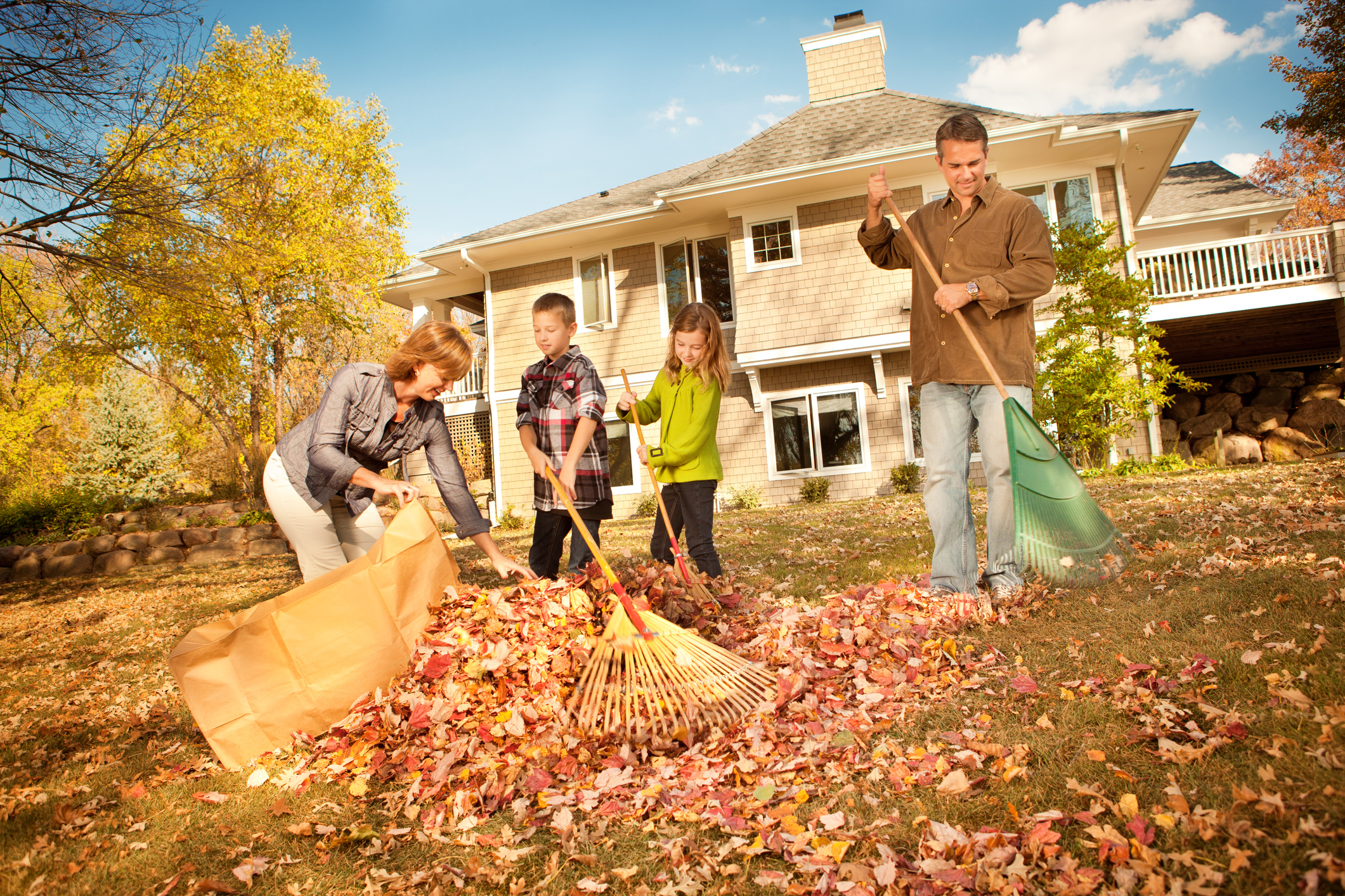 A mom, dad, daughter, and son raking leaves in front of their home in the fall
