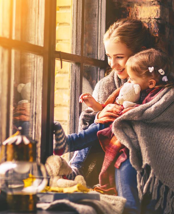 photo of a young mother holding her daughter near a window in fall