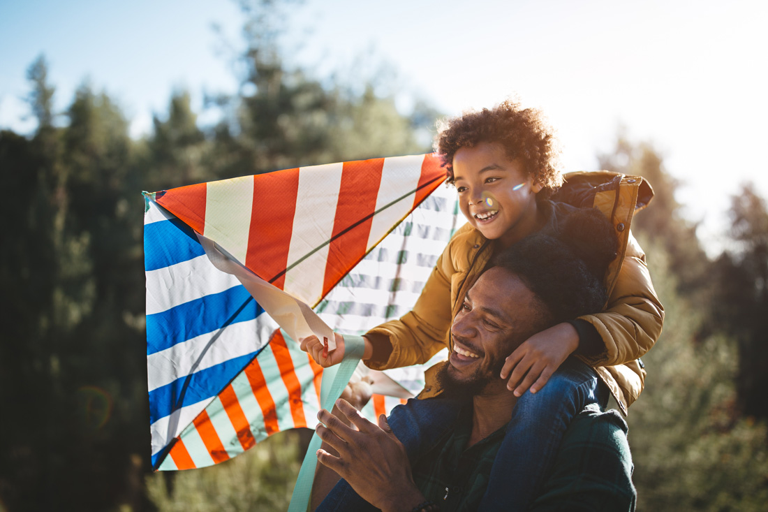 photo of a dad with his son on his shoulders and the son is flying a kite