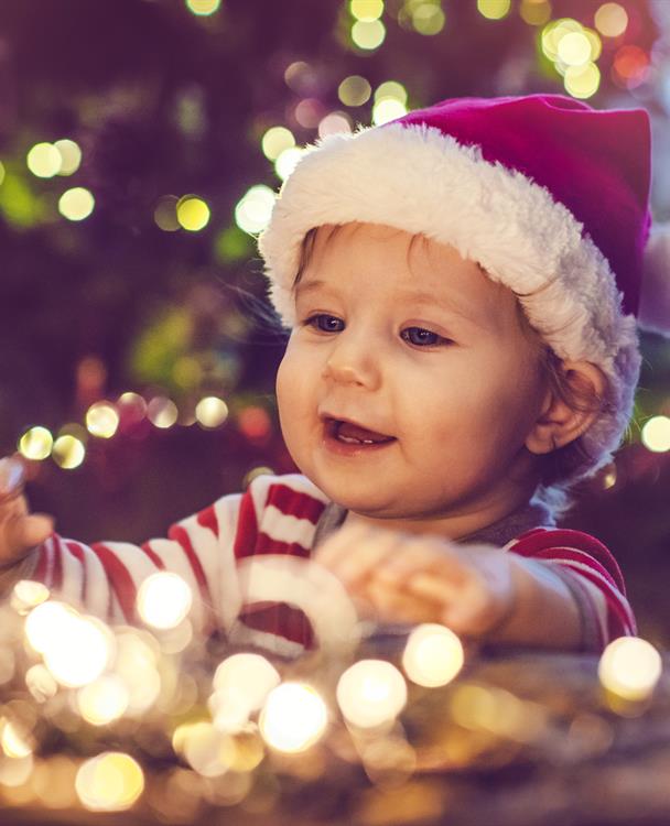 photo of a baby dressed in a Santa hat with a string of lights in front of him