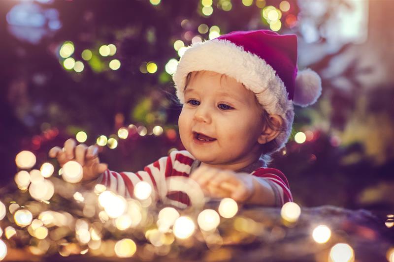 photo of a child wearing a red hat playing with a string of holiday lights