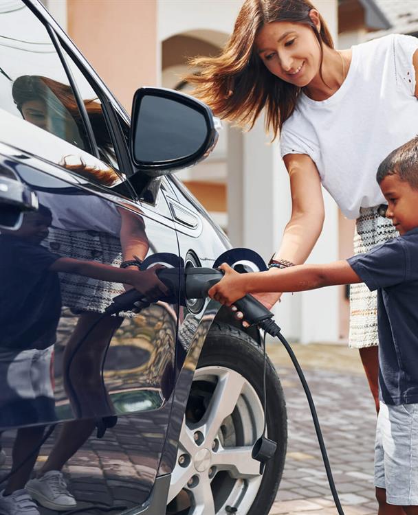 photo of a young boy plugging in a charger on an EV with help from his mom
