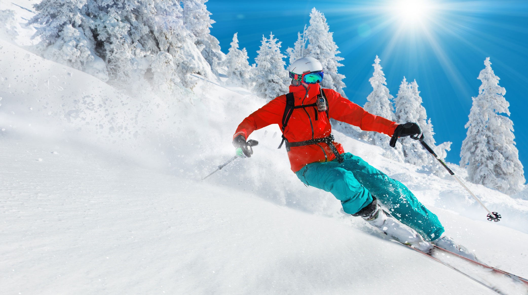 a man in warm gear skiing down a snowy hill on a sunny day