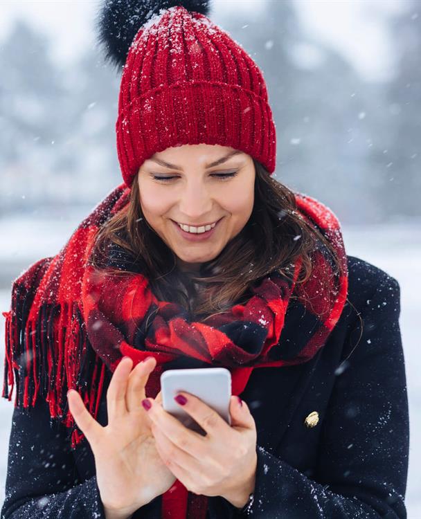 photo of a woman in a winter coat and hat using her mobile phone outside