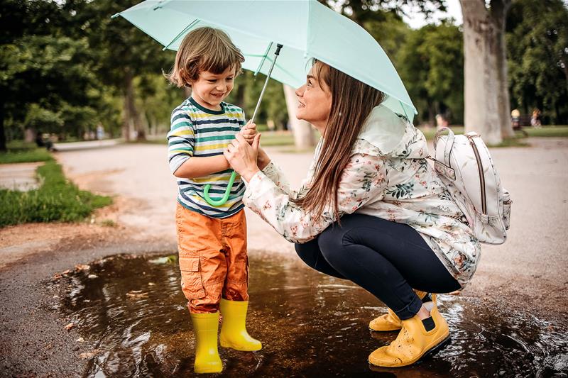photo of a young boy playing in a puddle while his mother holds an umbrella over him