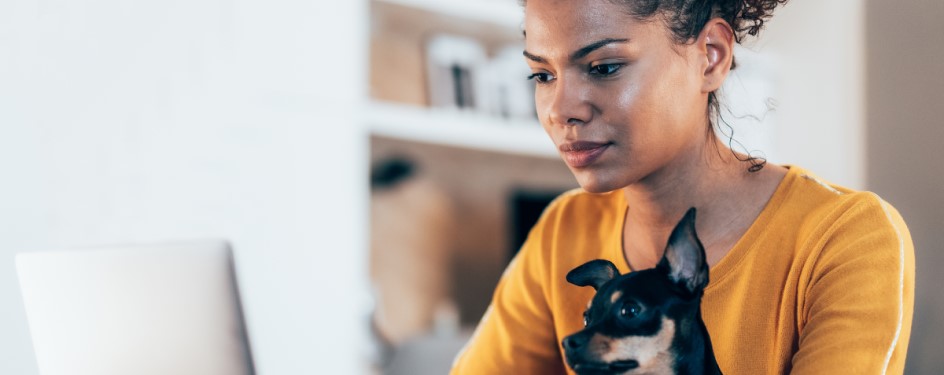 A girl looking at a computer holding a small dog