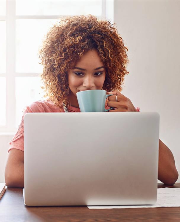 image of a woman looking at her laptop while holding a cup of coffee