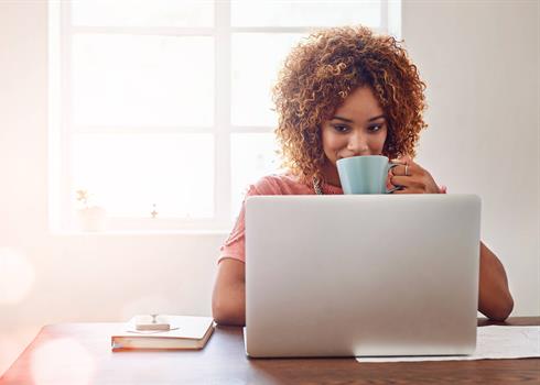 A woman looking at her laptop while holding a cup of coffee