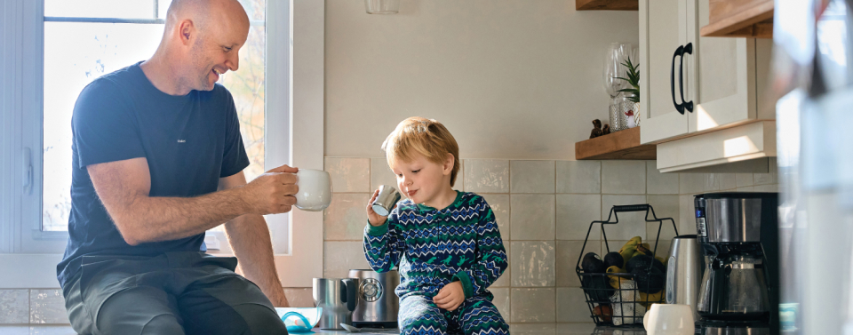 Father and son sitting on kitchen table sharing a drink together