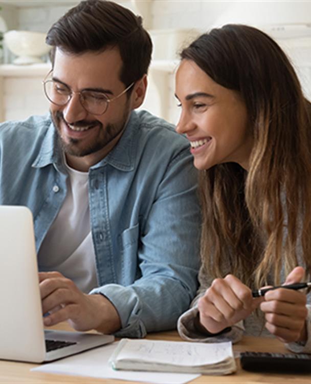 photo of a man and woman smiling as they look at their laptop computer