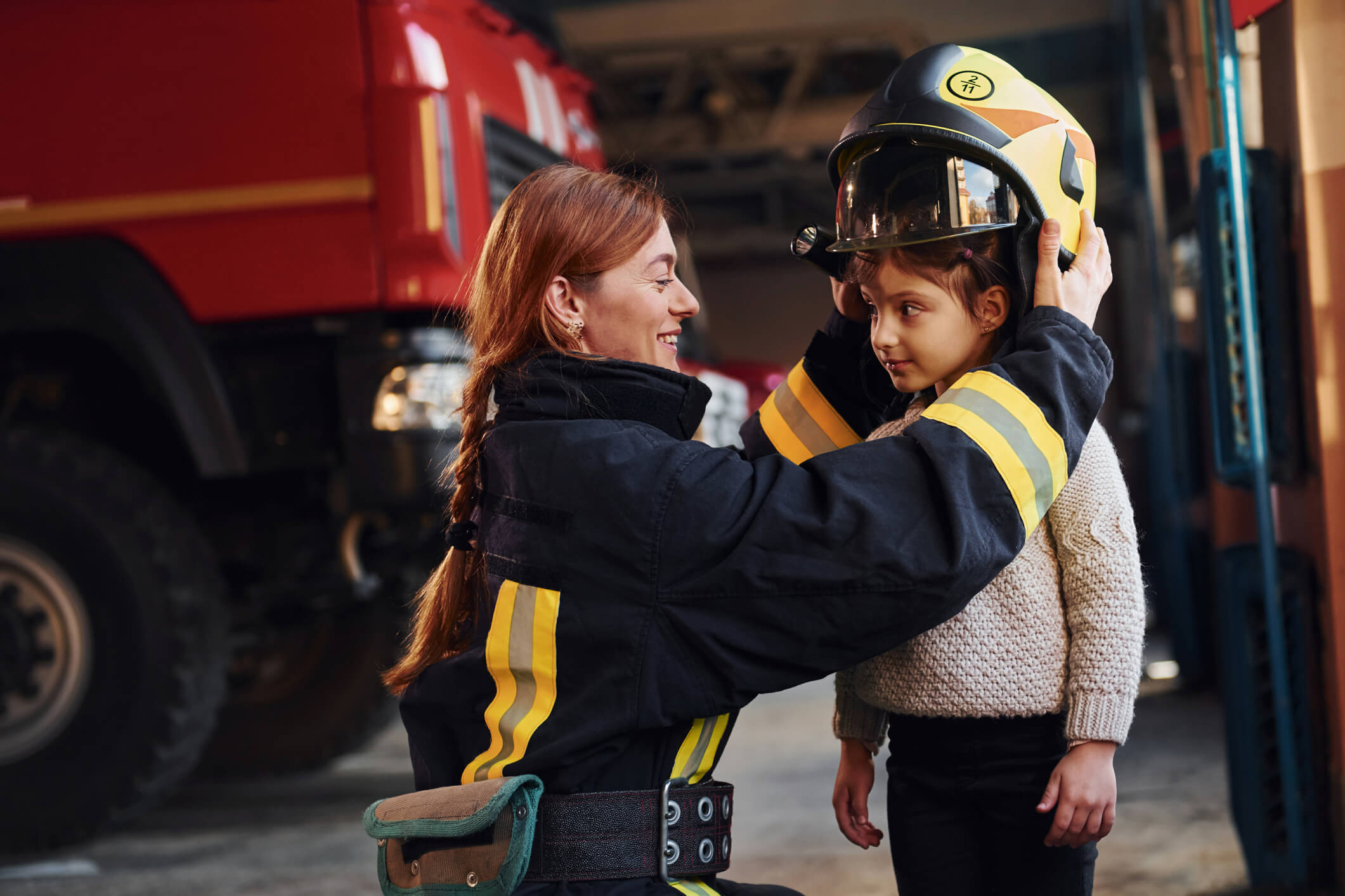 Child next to fire woman, getting a fire hat put on.