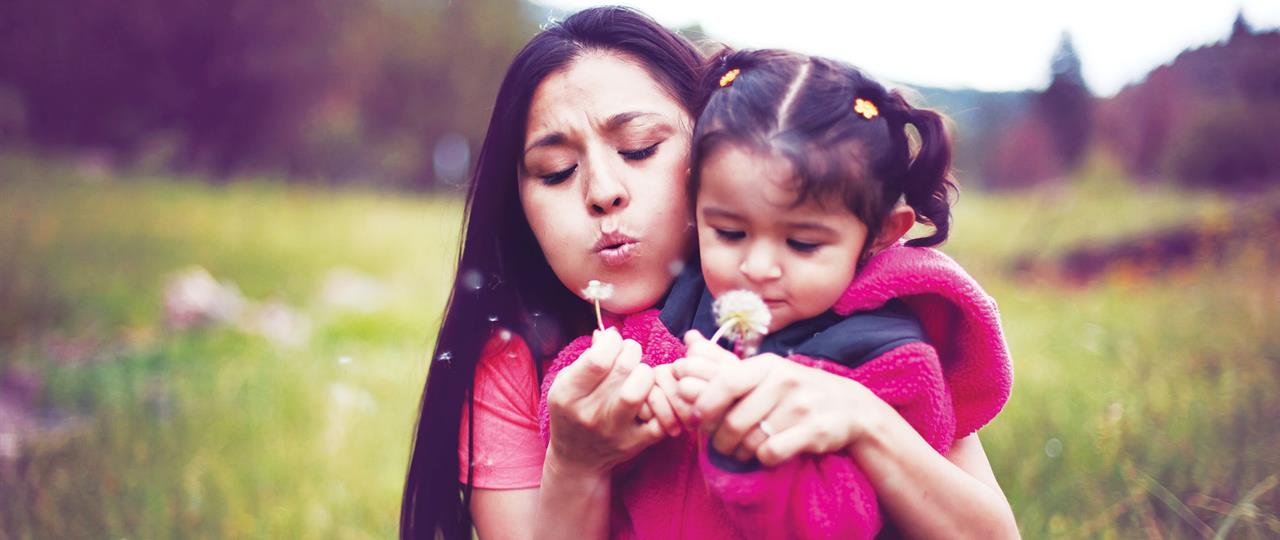 a mom and daughter blowing flowers in a field