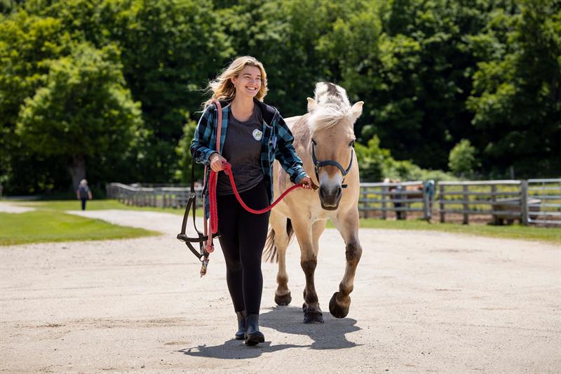 Photo of a smiling woman leading a horse at Hope Haven