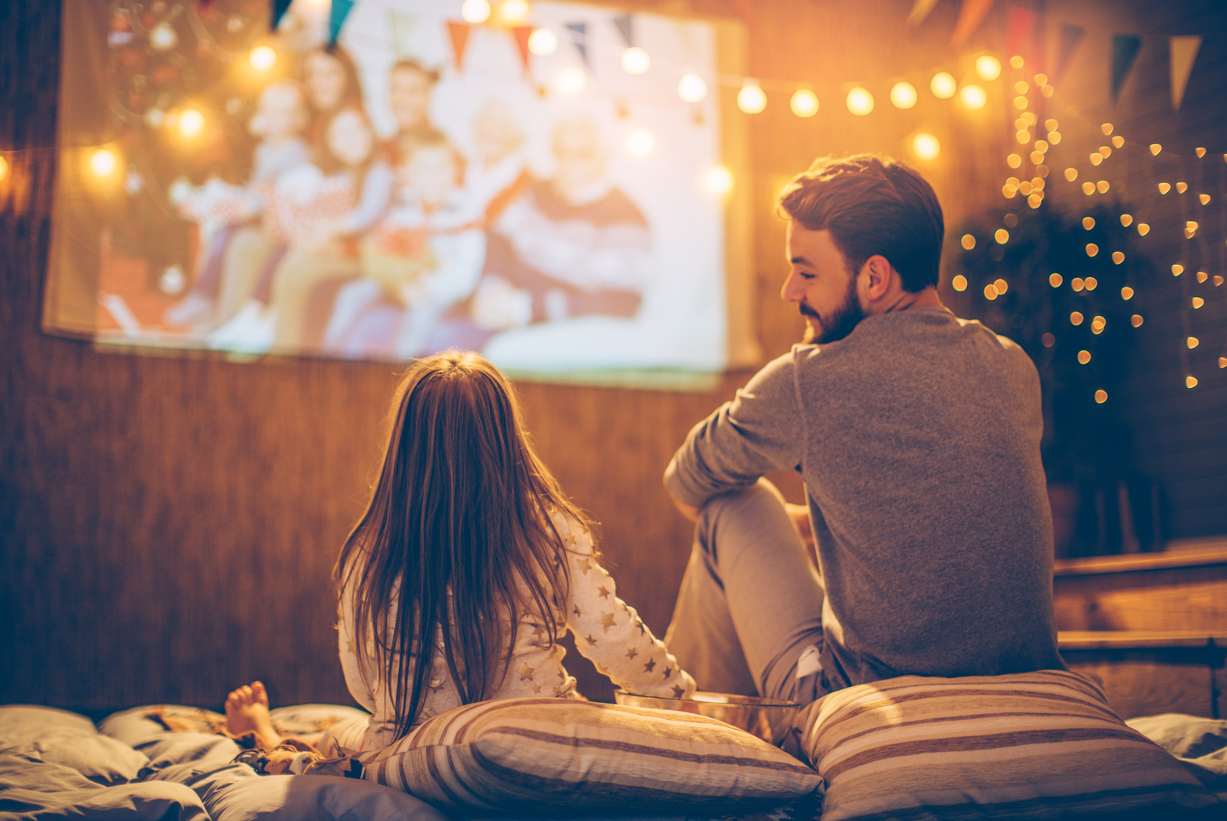 A father and daughter sitting outside on pillows watching a movie and talking