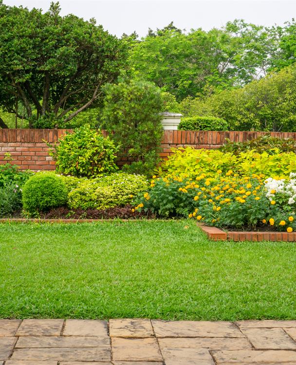 a green lawn and garden near a brick fence