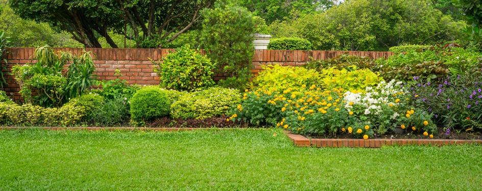 a green lawn and garden near a brick wall