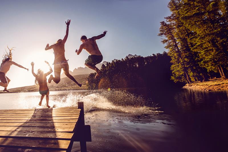 photo of teens jumping off of a dock into a lake at summer camp