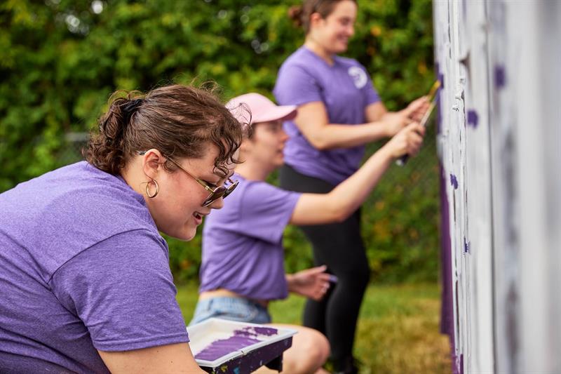 photo of three community volunteers painting a fence