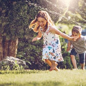 a young boy and girl running through a sprinkler on a lawn