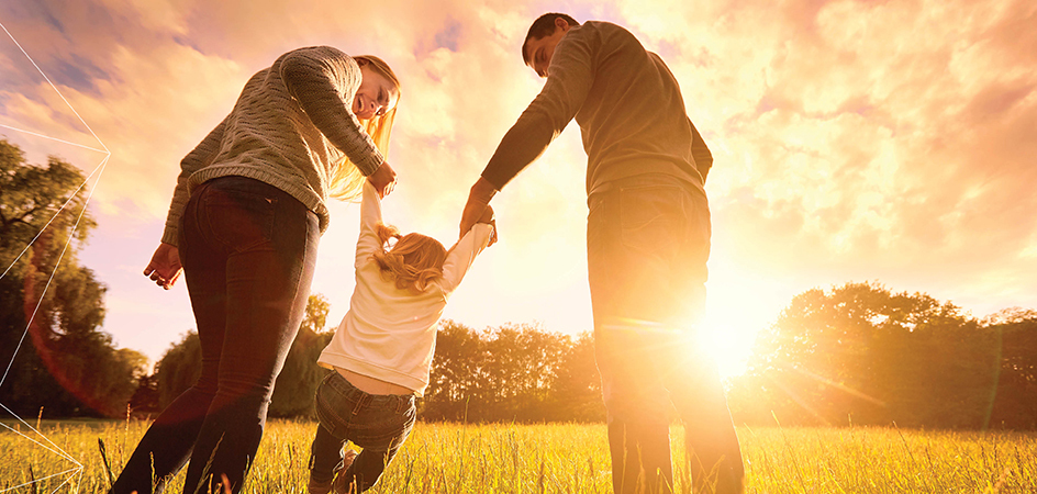 A mom and a dad holding their daughter's hand in a field