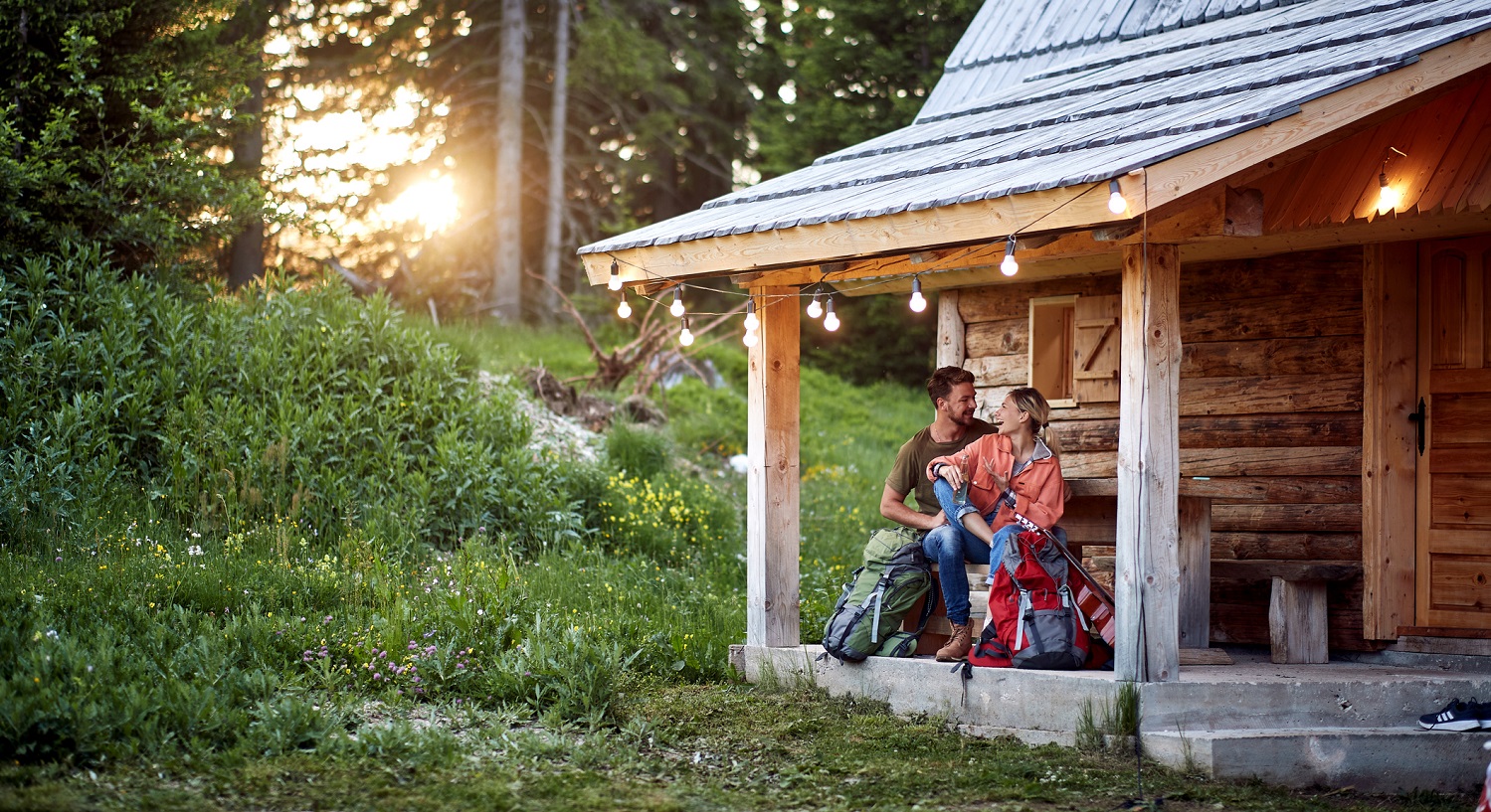 photo of a man and woman sitting on the front porch of their rustic cabin in the summer