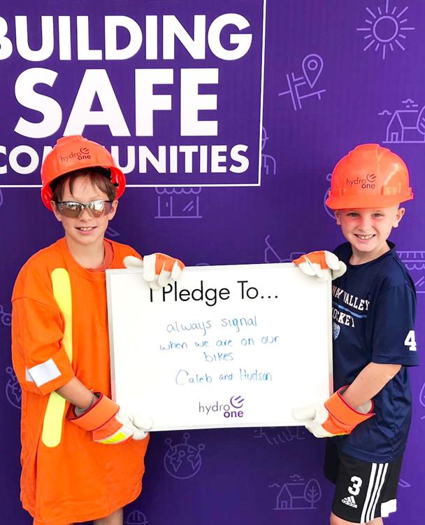 photo of two young boys wearing Hydro One safety gear and holding a sign committing to playing safe