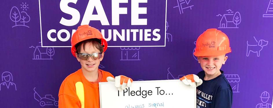 photo of two boys dressed in Hydro One safety gear standing in front of the Building Safe Communities pledge wall