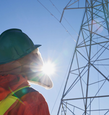 Utility worker in safety gear standing beside a high-voltage transmission tower and overhead power lines