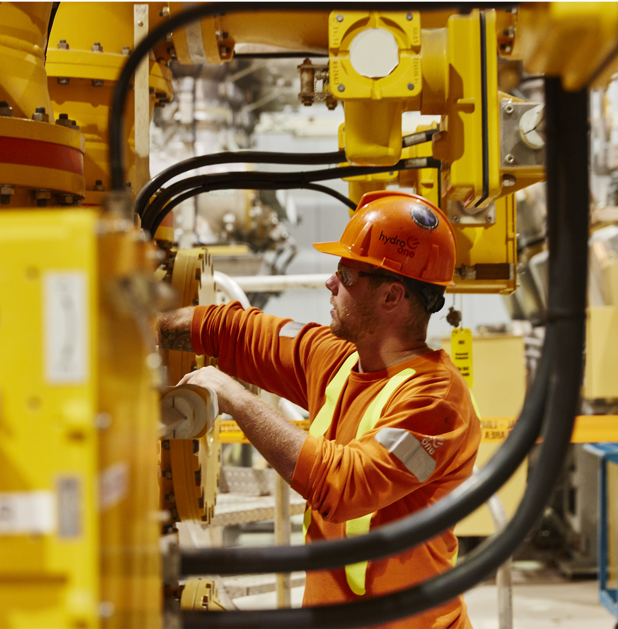 a worker in an orange hard hat and uniform looking at equipment