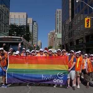 Photo of a group of Hydro One employees holding a large rainbow flag at a Pride event in Toronto