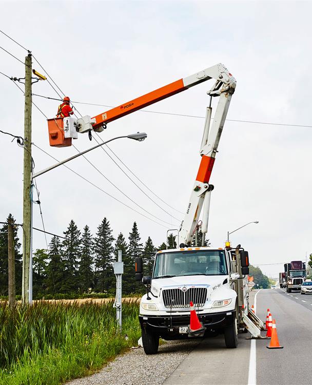 image of a Hydro One bucket truck parked on a street with a worker doing restoration work on a distribution pole