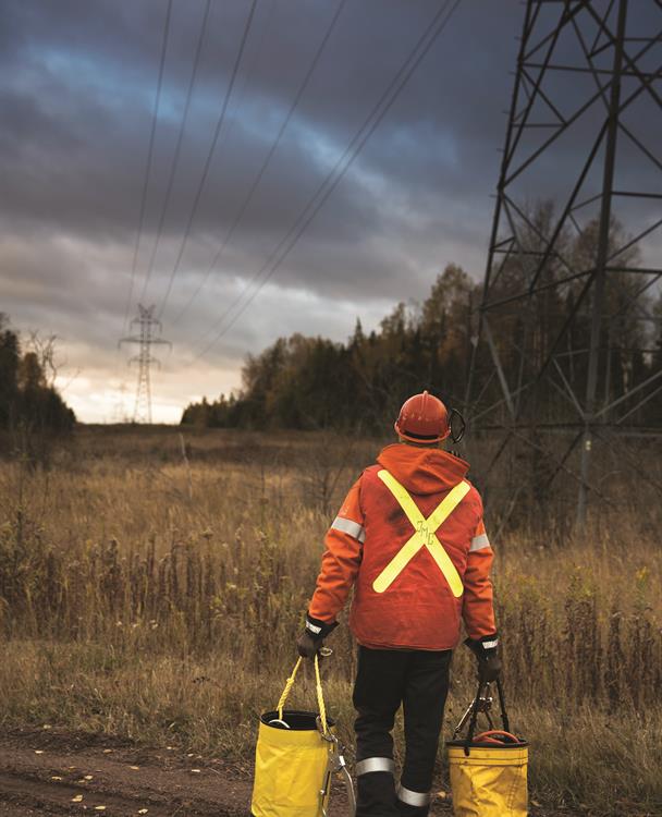 photo of a Hydro One worker carrying buckets on a Right of Way