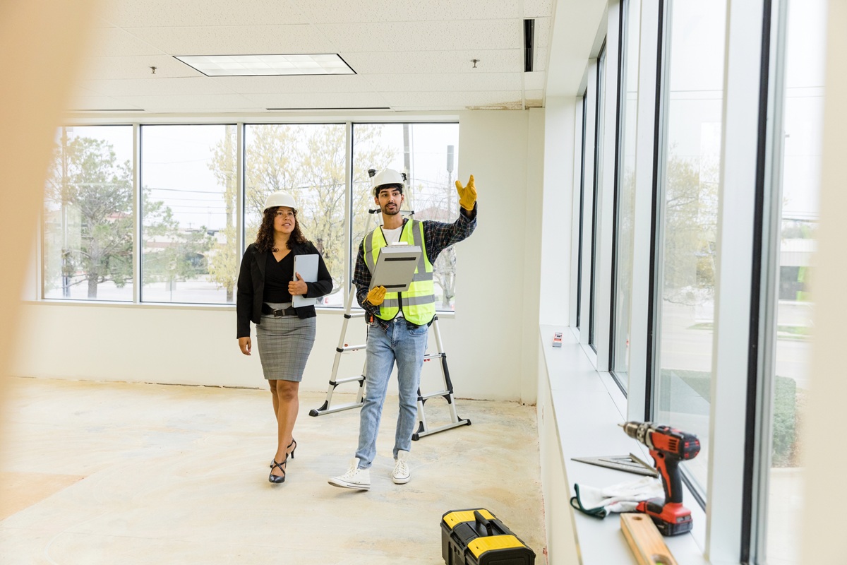 Two people walking through a bright office space wearing safety vests