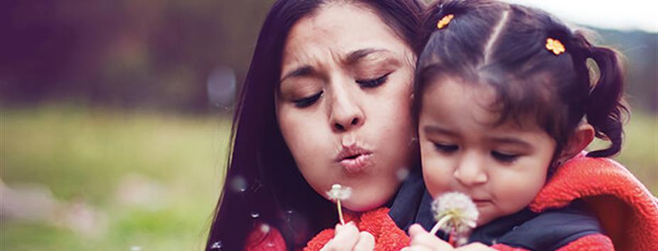 Photo of a woman and her daughter blowing dandelion petals