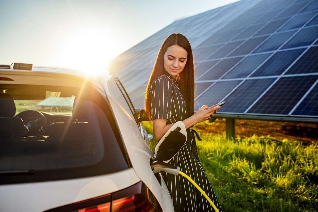 Woman waiting for electric car to charge and solar panels in background