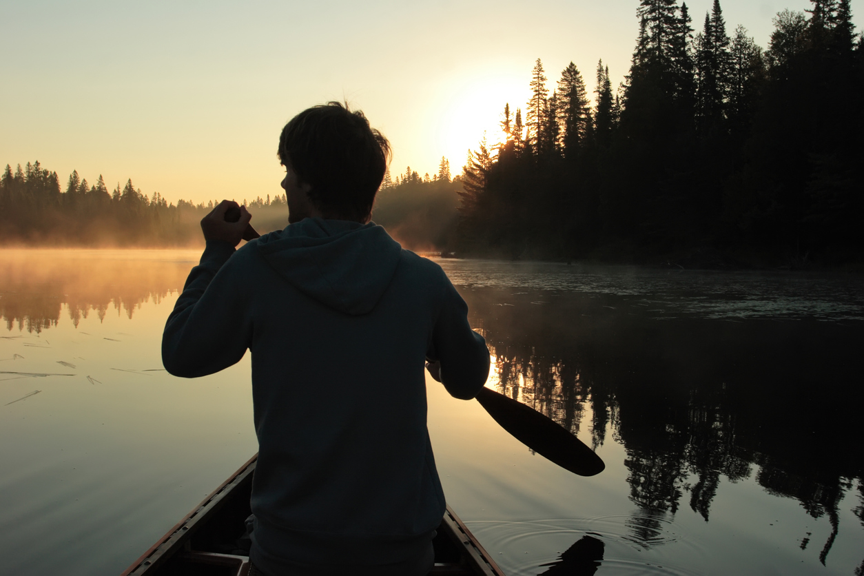 Young man canoeing at sunrise stock