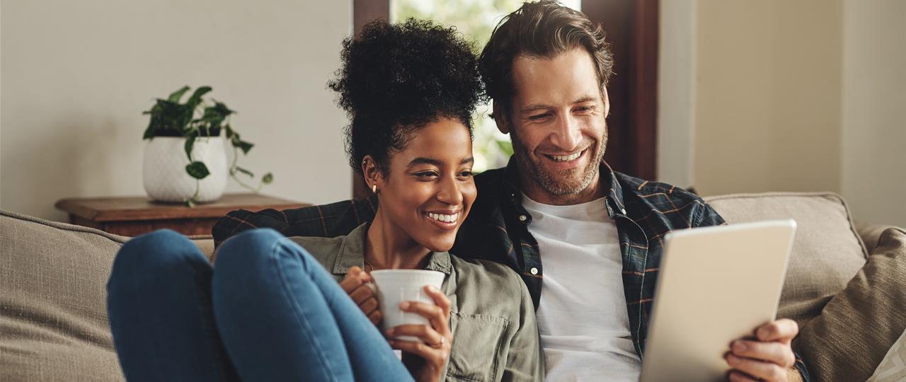 photo of a couple sitting on their couch looking at a tablet computer