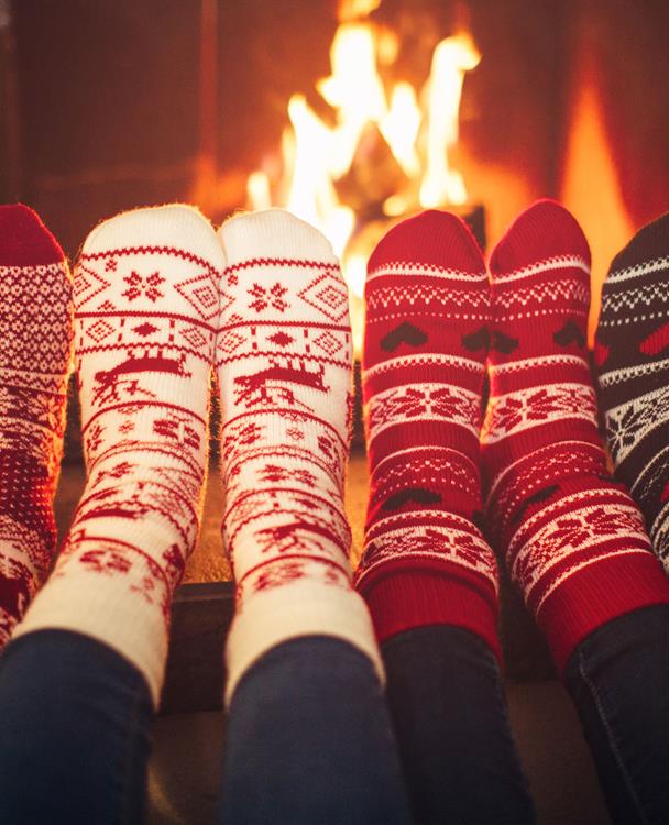 four sets of feet in holiday socks in front of a fire in a fireplace