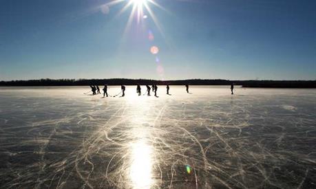 A group of people ice skating in the distance on a frozen lake