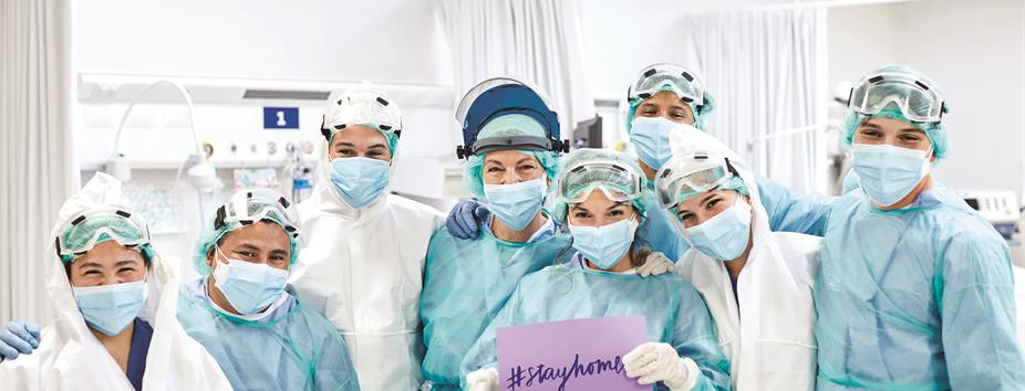 photo of nurses wearing scrubs holding a sign that says Stay Home