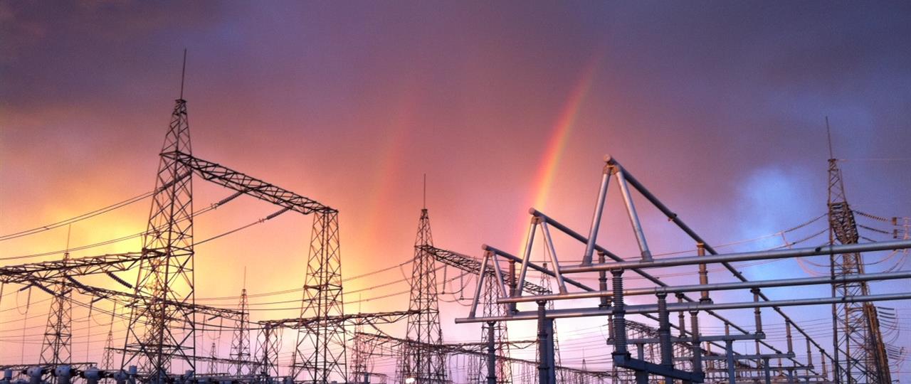 Photo of a Hydro One transmission station during a rain storm with a double rainbow behind it